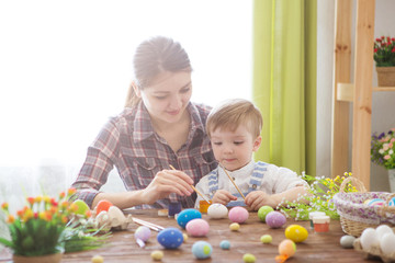 Wall Mural - Easter concept. Happy mother and her cute child getting ready for Easter by painting the eggs