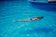 © katafree - Young slim woman in a black bikini swimsuit swims underwater in the pool