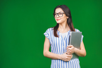 Young happy smiling woman in casual clothes holding laptop isolated over green background.