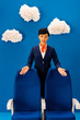 © LIGHTFIELD STUDIOS - smiling african american flight attendant pointing with hands at seats on blue background with clouds