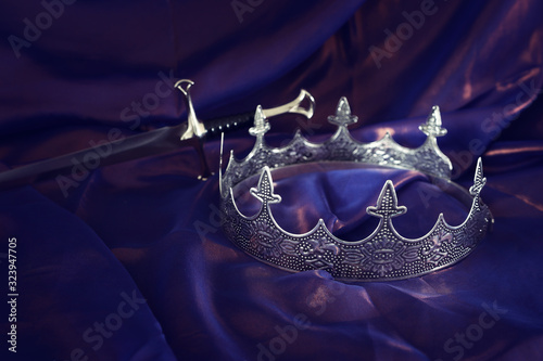Fotomural low key image of beautiful queen/king crown and sword over dark royal purple delicate silk