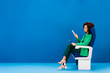 © LIGHTFIELD STUDIOS - side view of african american woman sitting on seat and holding smartphone on blue background