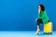 © LIGHTFIELD STUDIOS - pensive african american woman sitting on travel bag on blue background