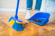 Latin man sweeping wooden floor with broom at home.