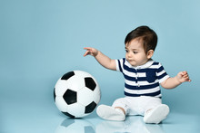 Toddler In Striped T-shirt, White Pants And Booties. He Is Looking Up, Sitting On Floor Against Blue Background. Close Up