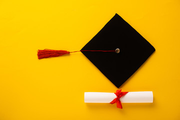 Wall Mural - Top view of diploma with beautiful bow and graduation cap with red tassel on yellow background