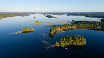 Wall Mural - Aerial view of blue lake with islands and green forests on a sunny summer evening in rural Finland. Drone photography.