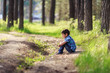 © Olga Gimaeva - little dark-haired boy sits on a forest path in a pine forest and thinks about something