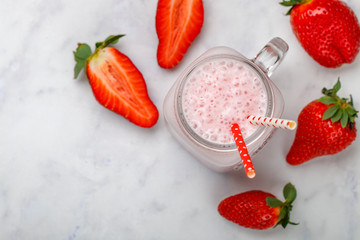 Wall Mural - smoothie or milkshake of fresh strawberries, yogurt or milk and ice cubes in Mason jar on a marble table. Concept of healthy vitamin drinks. Selective focus, top view, copy space