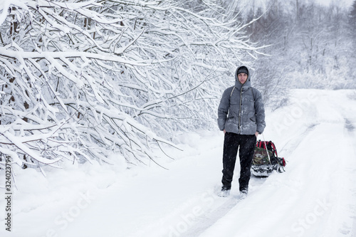 Adult man pulling sledge in the snow during strong snowfall Poster Mural XXL