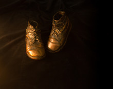 Low Key Image Of Bronzed Baby Shoes On A Dark Background