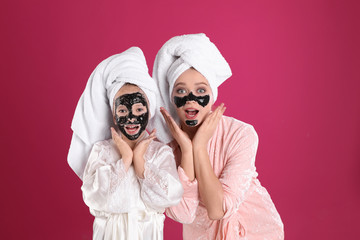 Poster - Emotional mother and daughter with black facial masks on pink background