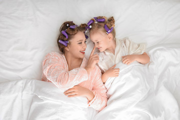 Canvas Print - Happy mother and daughter with curlers lying on bed, top view