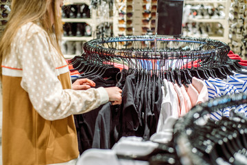 Shopping concept .teenager girl tries on and buys a sports shirt in the mall. A large selection of clothes in the store, black Friday sales. Showcase with sunglasses