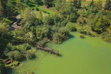 Aerial Photo Of A Beautiful Green Lake Surrounded With Trees, Walking Path And A Small Pier Protruding Into The Lake On A Sunny Day. People Standing On A Pier