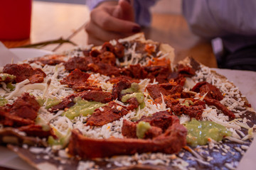 Woman eating delicious Mexican dish called tlayuda made of tortilla and meat