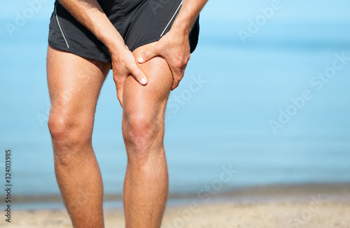Fotomural Sports injury muscle cramp pain fit runner man athlete holding painful thigh leg on outdoor summer jogging exercise