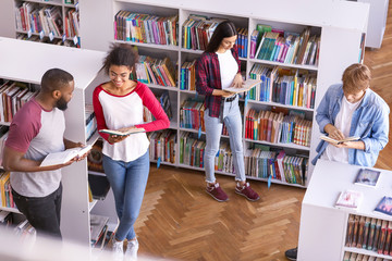 Wall Mural - Young students reading books while preparing for exam in library