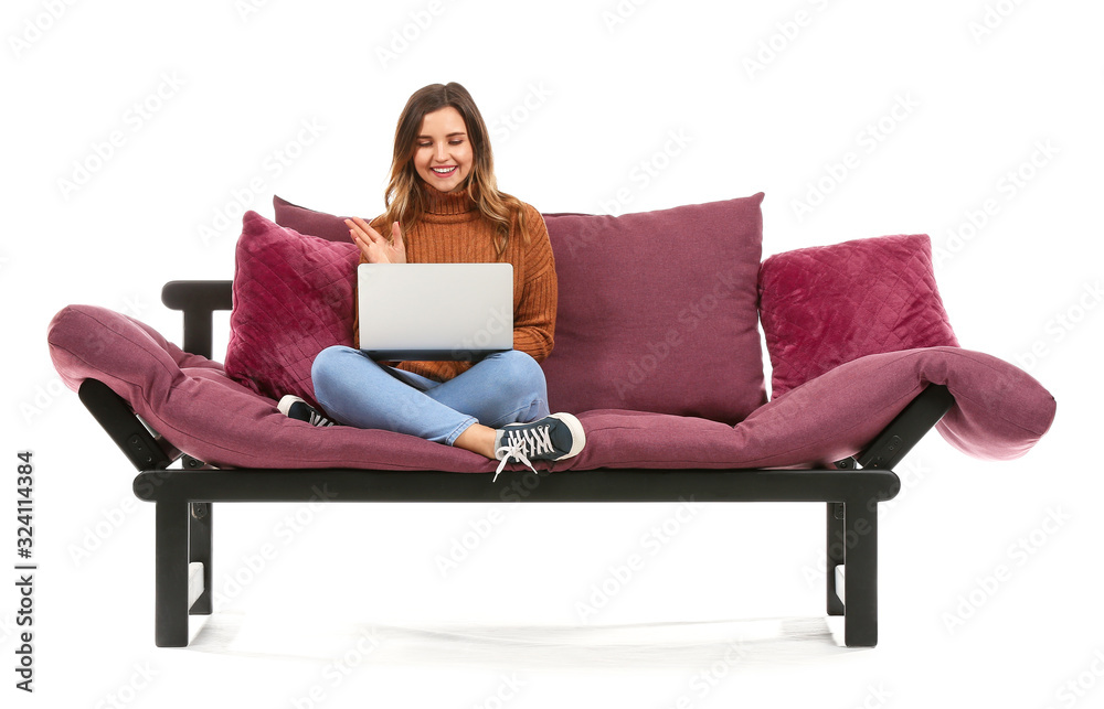 Young woman with laptop sitting on sofa against white background