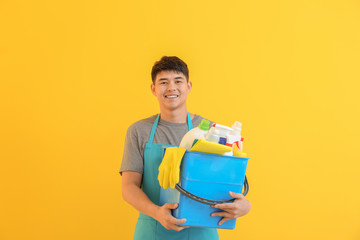 Canvas Print - Asian man with cleaning supplies on color background