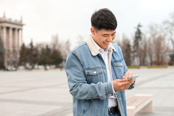 Poster - Young Asian man with mobile phone outdoors