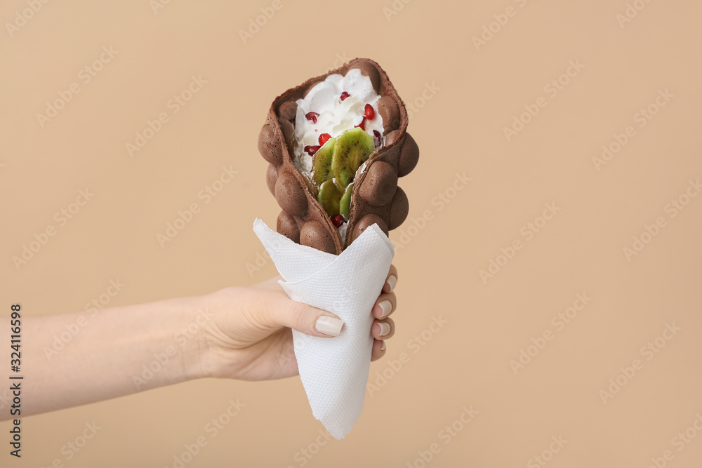 Female hand with delicious sweet bubble waffle on color background