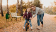 © Strelciuc - A cheerful young mother who is teaching her small and smiling daughter to ride the bike in a sunny autumn evening