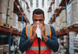 Young sick african warehouse worker blowing nose while working wearing safety vest