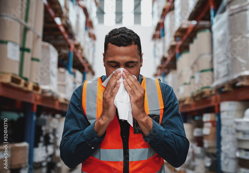 Fotomural Young sick african warehouse worker blowing nose while working wearing safety ve