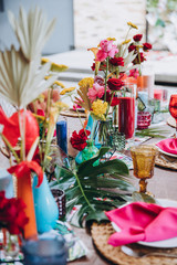 Banquet tables decorated in tropical style decor, dishes on the tables with pink napkins, glasses, candles, colorful flowers