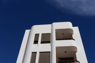 Contemporary white apartment building with art deco architectural style elements against blue sky