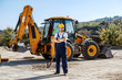 © Dusan Petkovic - Handsome caucasian worker in overall and helmet on head standing outdoors with crossed arms. In background is excavator.