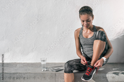 Runner woman tying running shoes laces wearing tech wearable technology smartwatch. Female athlete jogger using smart phone living a healthy active lifestyle drinking water.