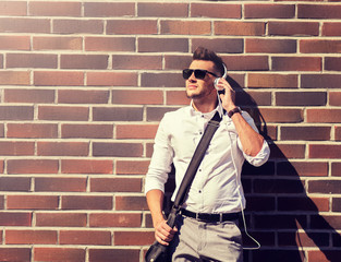 style, music, technology and people concept - happy smiling young man in headphones and sunglasses with bag over brickwall