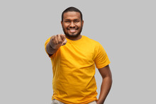 People Concept - Smiling Young African American Man In Yellow T-shirt Pointing To Camera Over Grey Background
