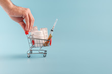 Male Hand Pushing Shopping Cart Full Of Pills On Blue Background Close Up.