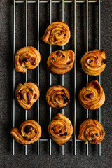 Canvas Print - Puff pastry snails with custard and raisins cooling down on a steel grate, deep grey background, shot from above