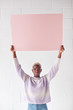 © Monkey Business - Happy Young Woman Holding Blank Pink Card With Copy Space Above Head White Against White Studio Wall