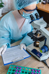 Female scientist studying coronavirus. The doctor looks through a microscope at a vaccine against coronavirus.