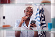 © Monkey Business - View Through Bathroom Cabinet Of Woman Brushing Teeth And Checking Phone Before Going To Work