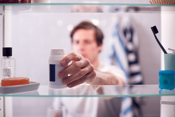 View Through Bathroom Cabinet Of Man Taking Medication From Container