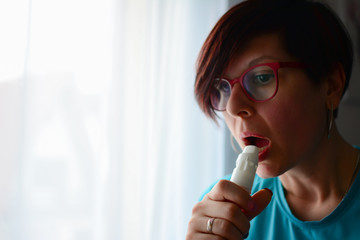 Attractive woman suffers a loss of breath and using asthma inhaler. Pretty woman taking her inhaler at home at the living room