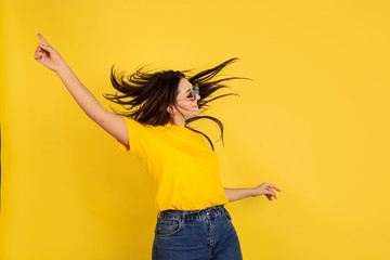 Poster - Inspired dancing in sunglasses. Caucasian woman on yellow studio background. Beautiful female brunette model in casual style. Concept of human emotions, facial expression, sales, ad, copyspace.