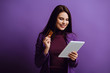 © LIGHTFIELD STUDIOS - smiling young woman looking at digital tablet while holding credit card on purple background