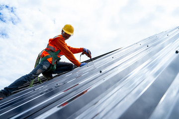 Poster - Roofer worker in protective uniform installing metal sheet on top of the new roof,Concept of house under construction.