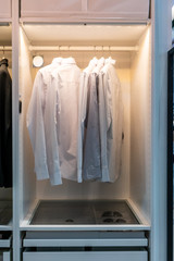 White and gray basic shirts hanging in walk in closet with drawer