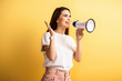happy girl speaking in megaphone while standing with open arm and looking away on yellow background