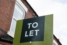 UK United Kingdom Green Lettings To Let Rental Property Sign With Red Brick House In Background. Landlord Investment Property Portfolio Real Estate British England Concept Idea