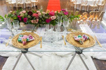 Two table settings with golden plates for a bride and groom on a glass table