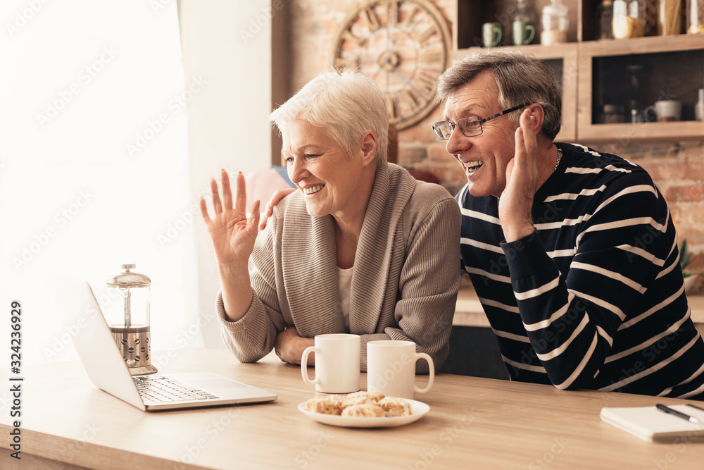 Happy senior couple looking at laptop screen in kitchen and waving - obrazy, fototapety, plakaty 